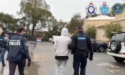 Australian police walk a hooded figure away.