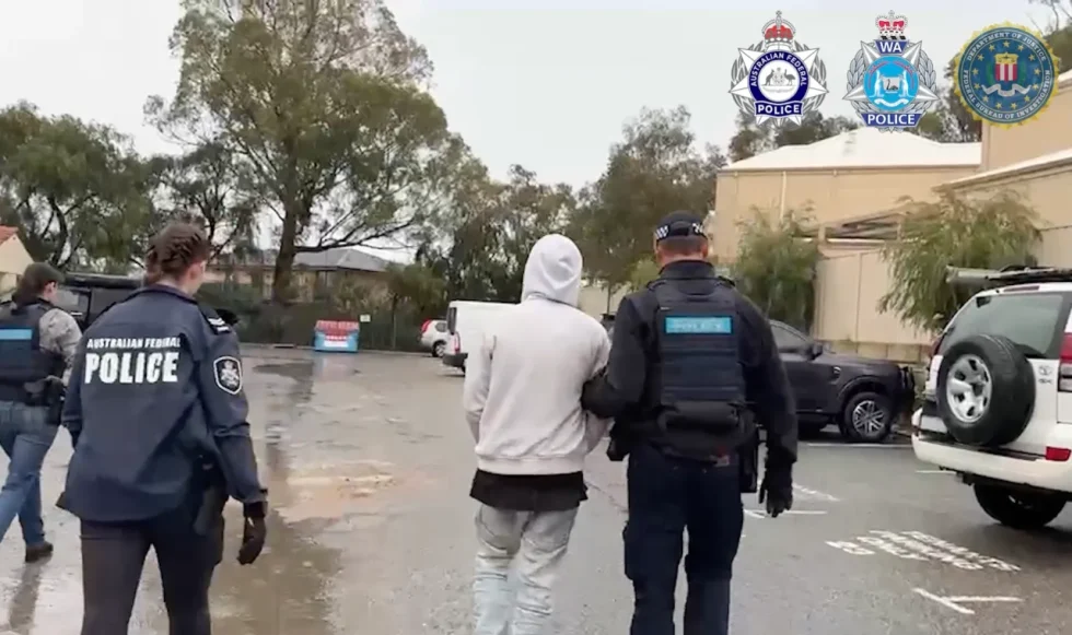 Australian police walk a hooded figure away.